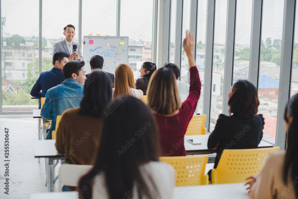 Obraz premium Asian male speaker is speaking at seminars and workshops to the people in the meeting. Participants are raising their hands to ask questions.