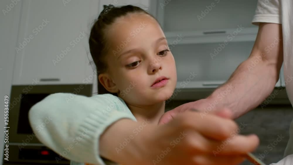 Close up shot of cute little girl of elementary school age spreading tomato sauce on pizza crust when cooking with father in kitchen Close up shot of cute little girl of elementary school age spreading tomato sauce on pizza crust when cooking with father in kitchen