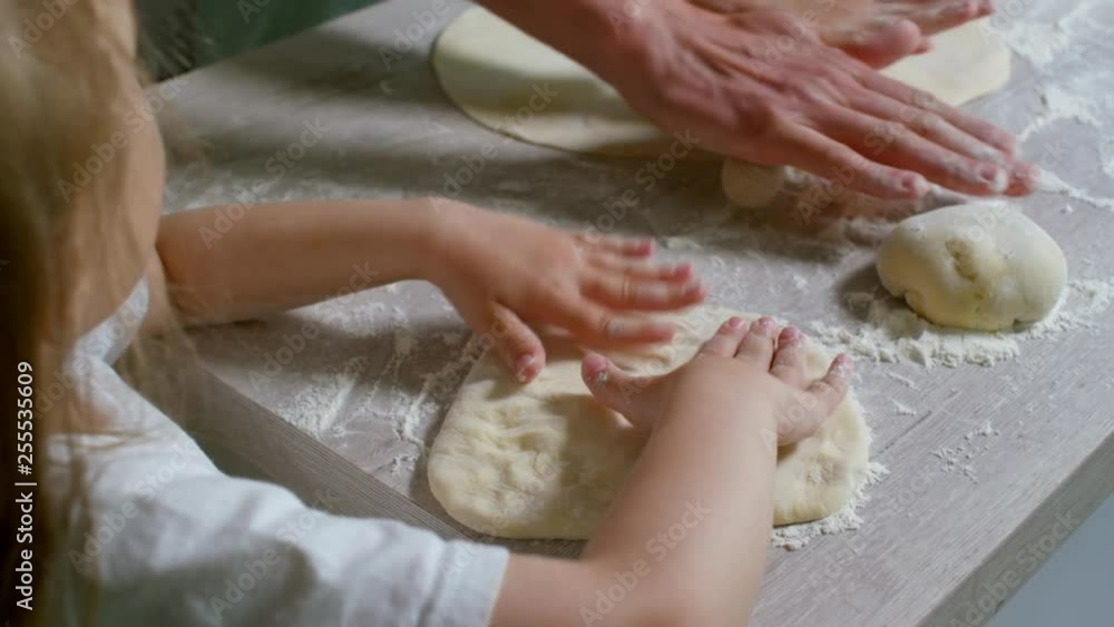 Close up shot of cute little girl and her father making dough together in kitchen, father rolling it out on floured surface Close up shot of cute little girl and her father making dough together in kitchen, father rolling it out on floured surface