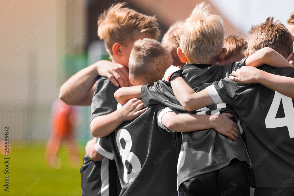 Fototapeta Junior football team stacking hands before school tournament match. Young boys soccer players in black shirts huddling before the final game