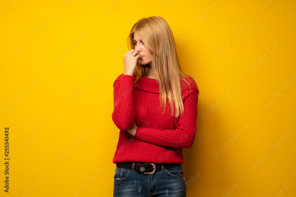 Blonde woman over yellow wall having doubts Blonde woman over yellow wall having doubts