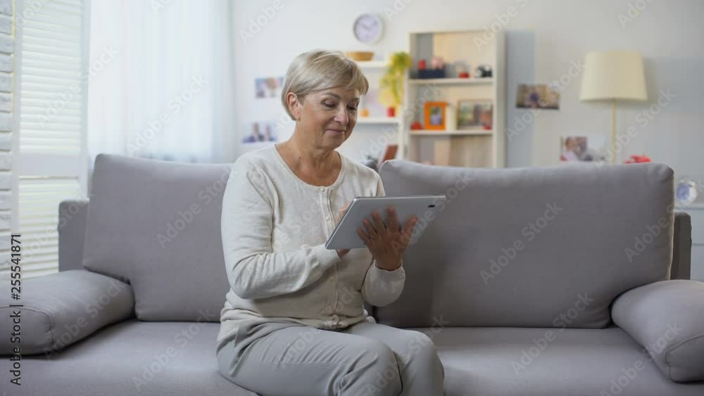 Senior lady shopping online on tablet at home smiling at camera, technology Senior lady shopping online on tablet at home smiling at camera, technology