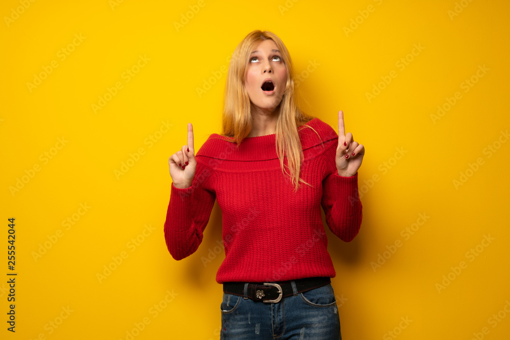 Blonde woman over yellow wall surprised and pointing up Blonde woman over yellow wall surprised and pointing up