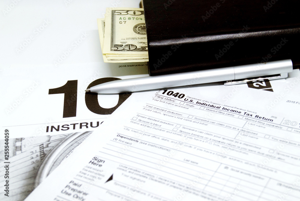 Income tax form with instruction, notebook with dollars and pen.