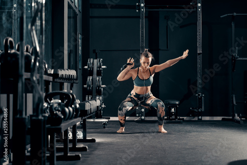 Caucasian muscular brunette with earphones in ears doing workouts with kettlebell in squat position. Night workout in gym concept.