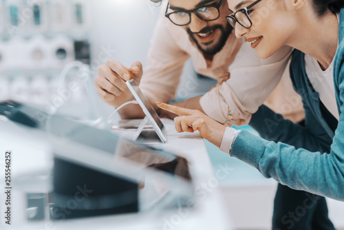 Εκτύπωση καμβά Young attractive multicultural couple with eyeglasses trying out tablet in tech store