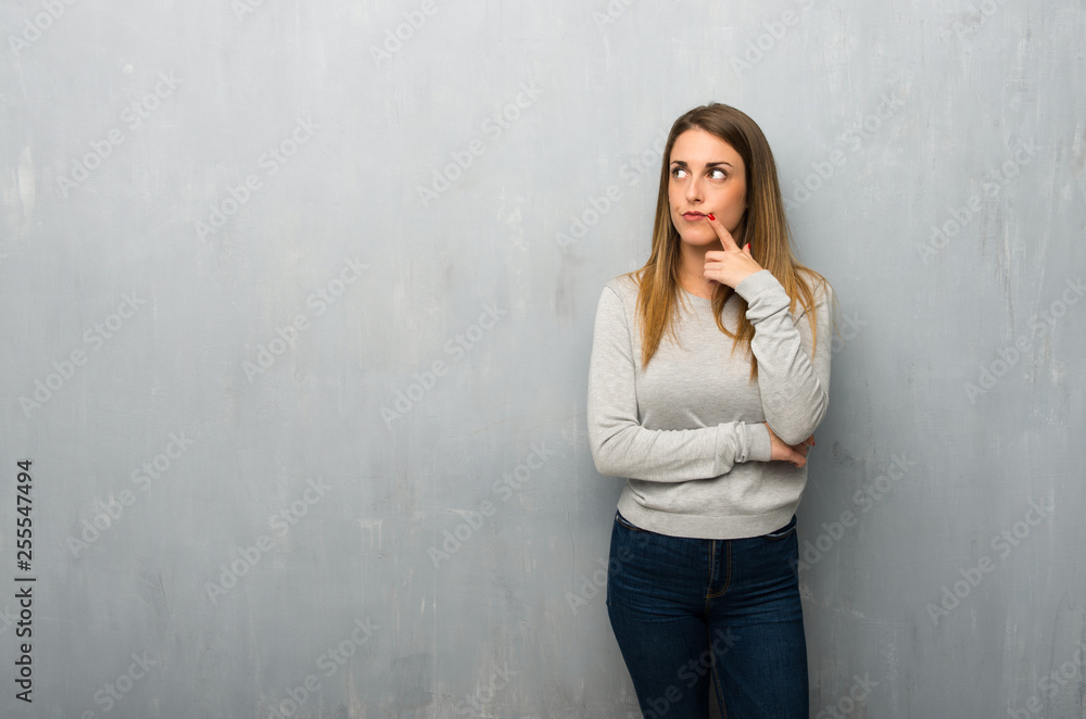 Young woman on textured wall having doubts while looking up