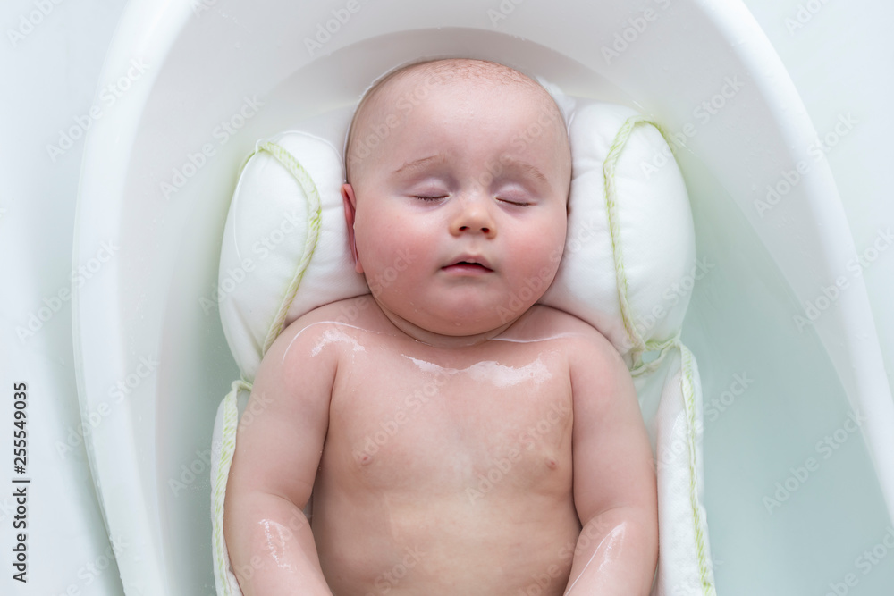 Cute adorable six months baby boy is sleeping in the baby bathtub on a