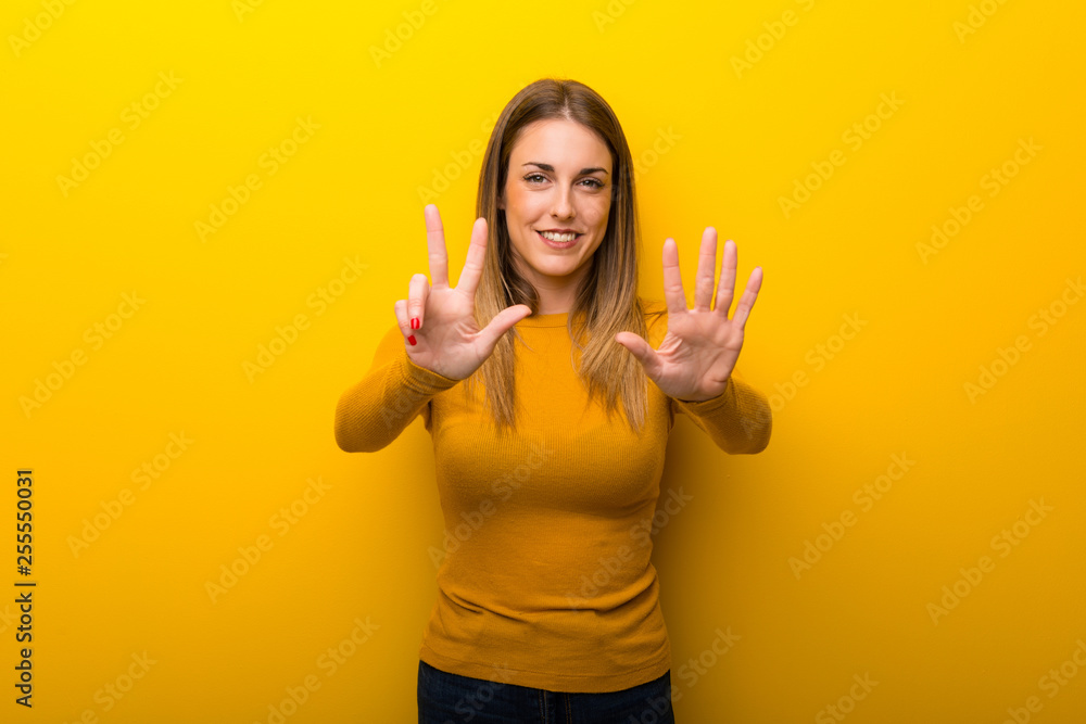 Young woman on yellow background counting eight with fingers Young woman on yellow background counting eight with fingers