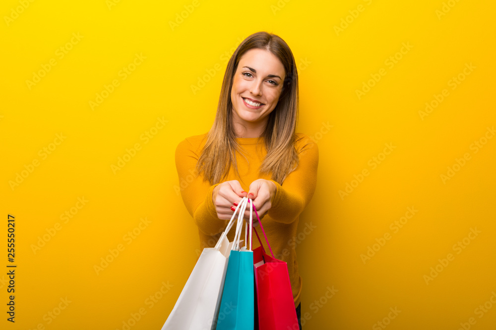 Young woman on yellow background holding a lot of shopping bags