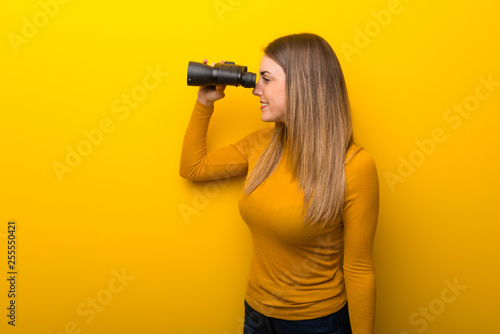 Young woman on yellow background and looking in the distance with binoculars © luismolinero