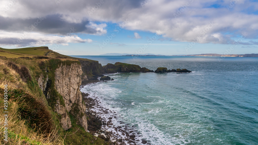 Stunning rugged coastal landscape with sheer cliffs rising from the Atlantic Ocean waters under a dramatic winter day sky. County Antrim scenic coastline, Northern Ireland