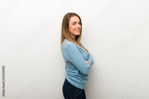 Blonde woman on isolated white background keeping the arms crossed in lateral position while smiling