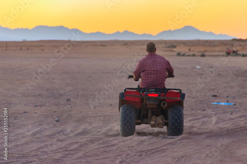Young man in safari trip through egyptian desert driving ATV at sunset. Quad bikes safari in the desert near Hurghada, Egypt