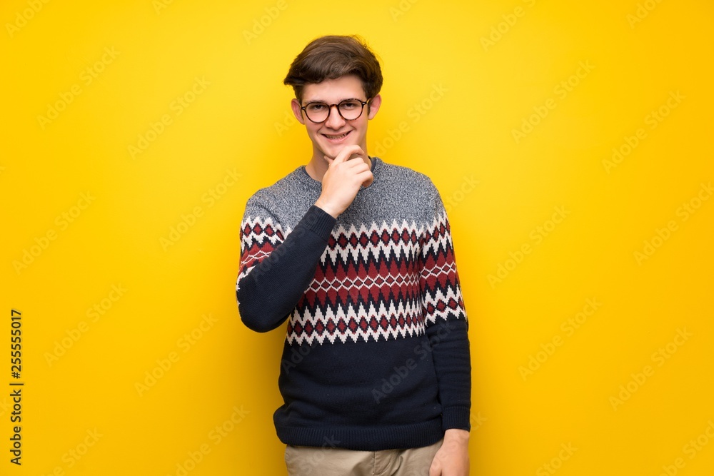 Teenager man over yellow wall with glasses and smiling Teenager man over yellow wall with glasses and smiling
