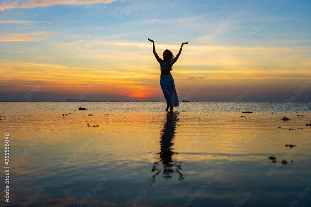 Young beauty girl dancing at tropical beach on sea water at paradise island at sunset. Summer concept. Holiday travel.