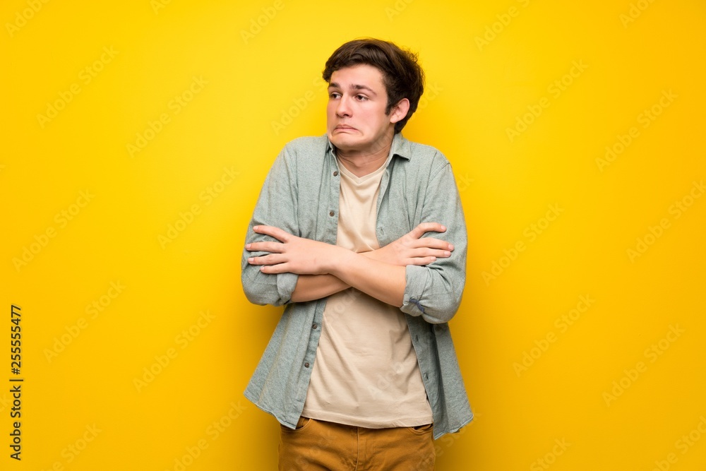 Teenager man over yellow wall making doubts gesture while lifting the shoulders Teenager man over yellow wall making doubts gesture while lifting the shoulders