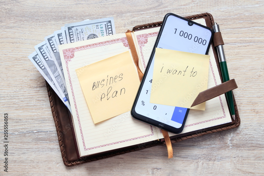 organizer with us dollars and open calculator with numbers 1 000 000 and a sticky note sheet with an inscription Busines Plan, I Want To, on the background of a desk organizer with us dollars and open calculator with numbers 1 000 000 and a sticky note sheet with an inscription Busines Plan, I Want To, on the background of a desk