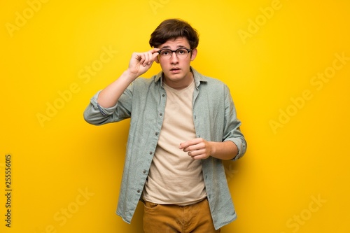 Teenager man over yellow wall with glasses and surprised © luismolinero