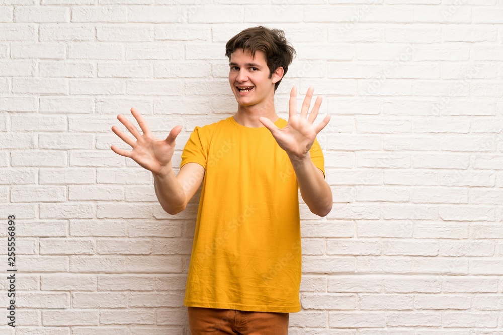 Teenager man over white brick wall counting ten with fingers Teenager man over white brick wall counting ten with fingers