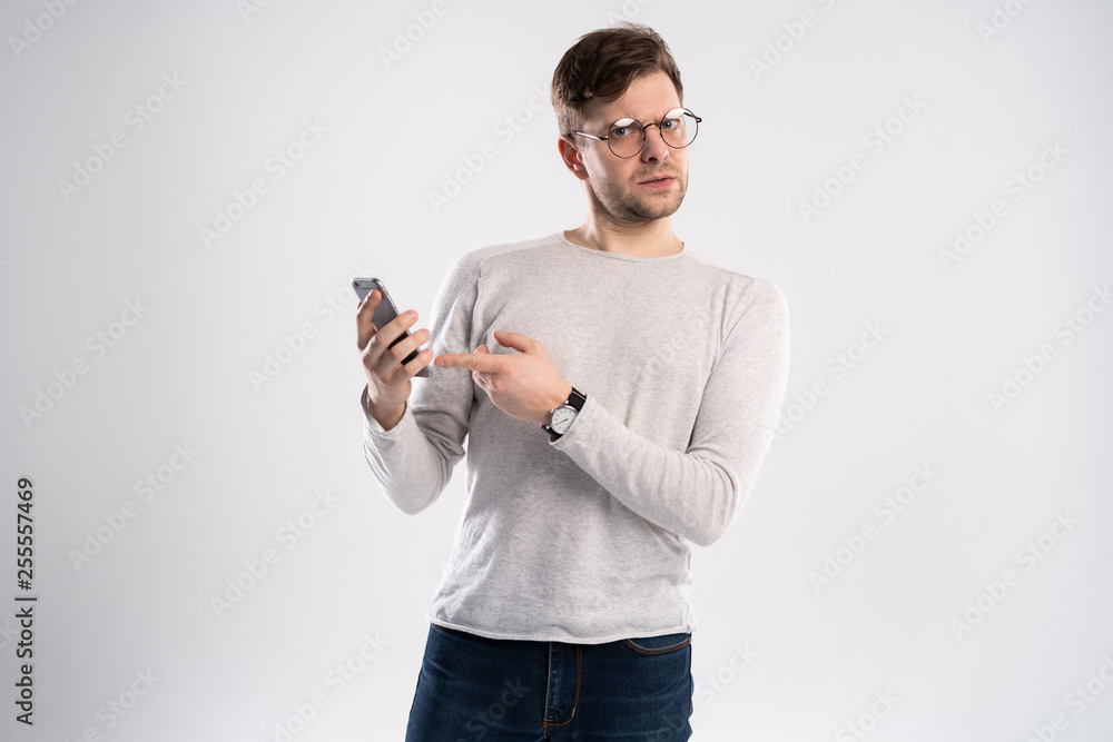 Close up portrait of handsome young man in white t-shirt, holding smartphone, looking scared and confused reading text message or e-mail. Close up portrait of handsome young man in white t-shirt, holding smartphone, looking scared and confused reading text message or e-mail.