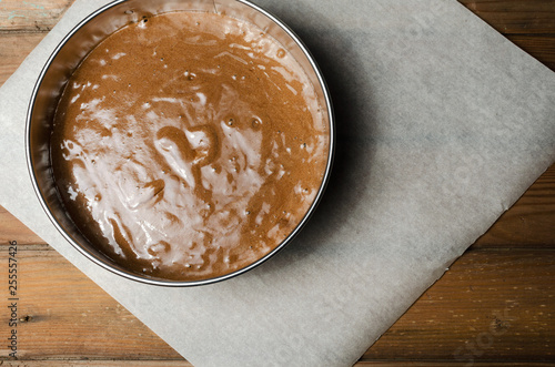 Cake pan with chocolate batter and wooden spoon close up on dark wooden background.