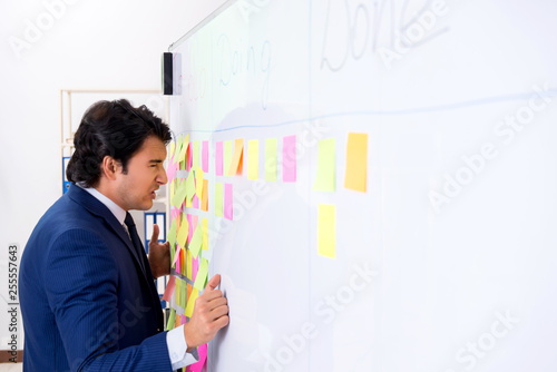 Young handsome employee in front of whiteboard with to-do list 