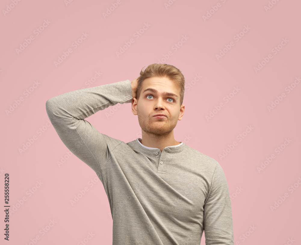 A thoughtful man holds his hand on the back of his head, looks thoughtfully upward. Isolated on pink background with copy space for text A thoughtful man holds his hand on the back of his head, looks thoughtfully upward. Isolated on pink background with copy space for text