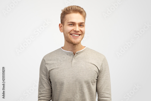 Portrait of enthusiastic man, smiles broadly, laugh joyfully at funny rumor, wears casual clothes. Content student has break after classes indoor. Isolated on white background