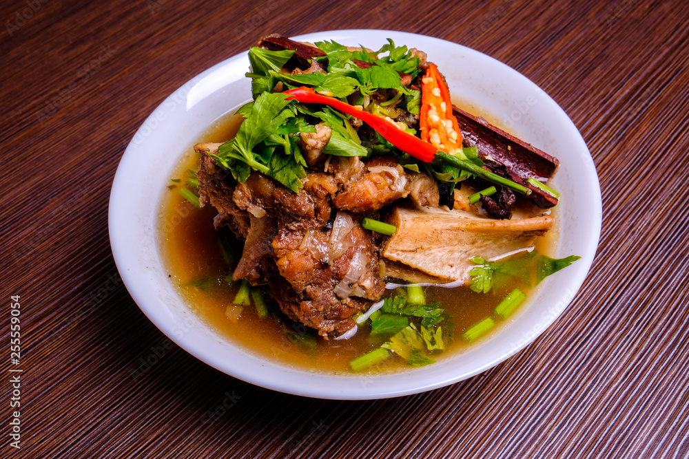 Cow bone soup or Sup Tulang in Malay . Muslim food in white bowl on dark brown wooden plate . Selective focus . Cow bone soup or Sup Tulang in Malay . Muslim food in white bowl on dark brown wooden plate . Selective focus .