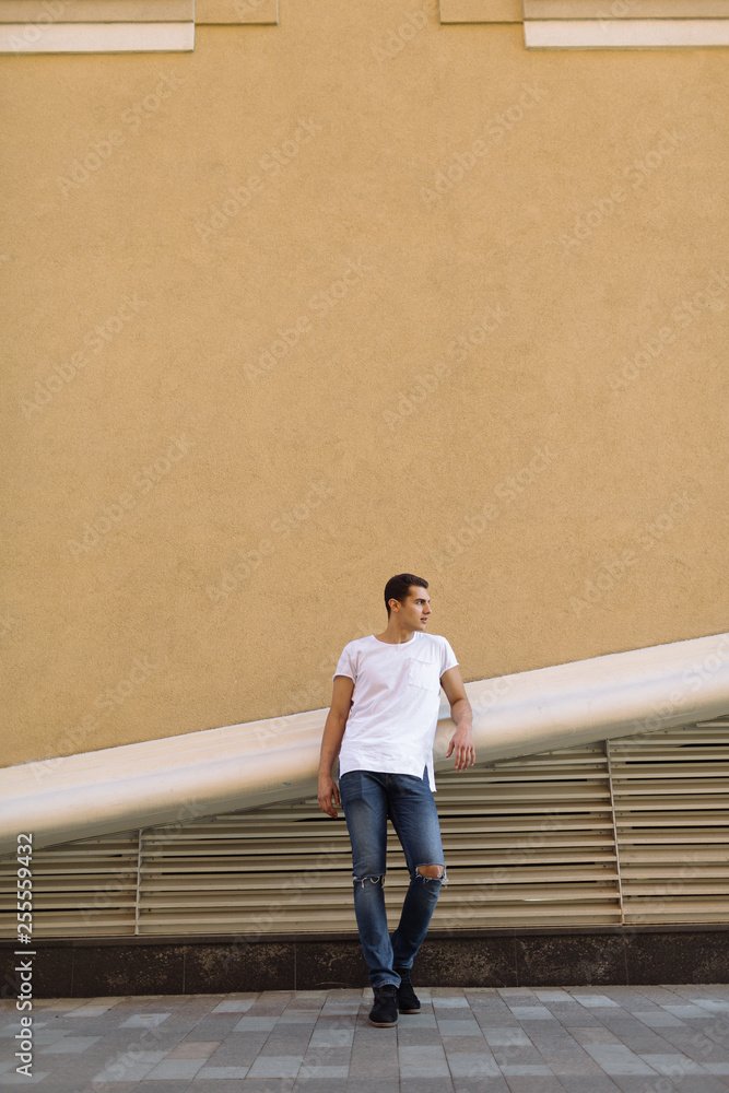 Beautiful caucasian man in white t-shirt and blue jeans stay on the street Beautiful caucasian man in white t-shirt and blue jeans stay on the street