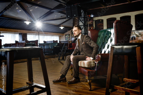 stylish man in a suit sits in a chair in a pub