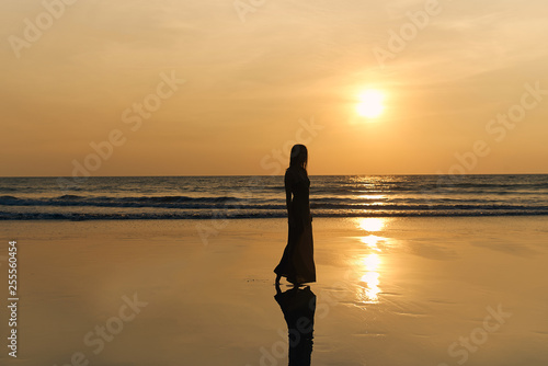 Contrast silhouette of a young slender woman against the background of a Sunny sunset  the sea and the sandy beach. Warm evening tones and reflections of the figure on the wet sand