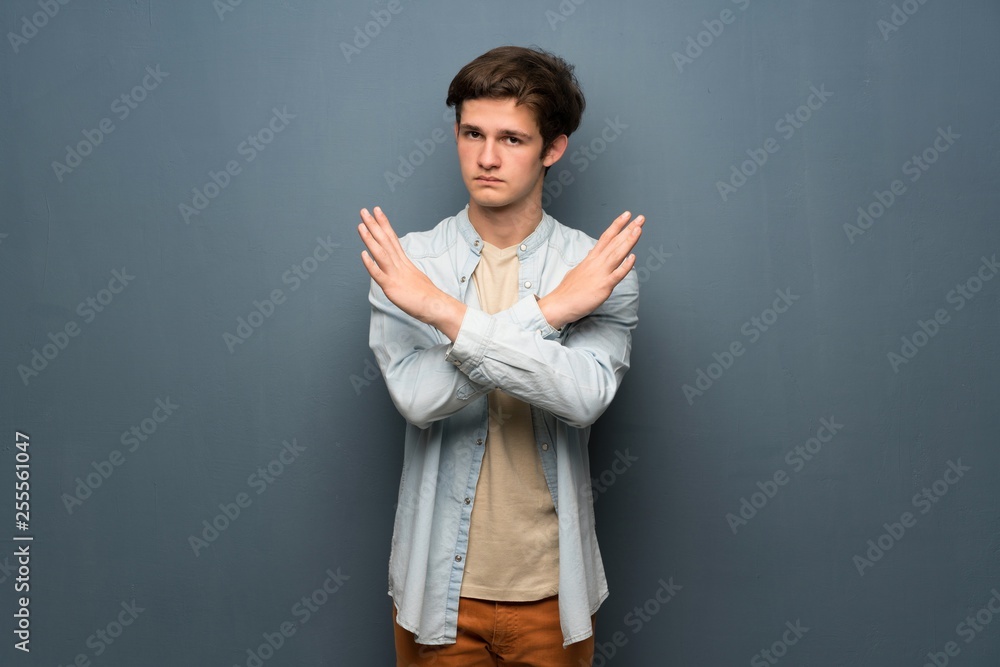Teenager man with jean jacket over grey wall making NO gesture Teenager man with jean jacket over grey wall making NO gesture