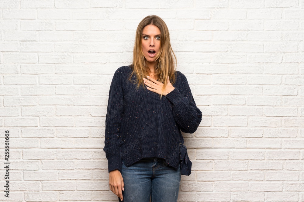 Blonde woman over brick wall surprised and shocked while looking right