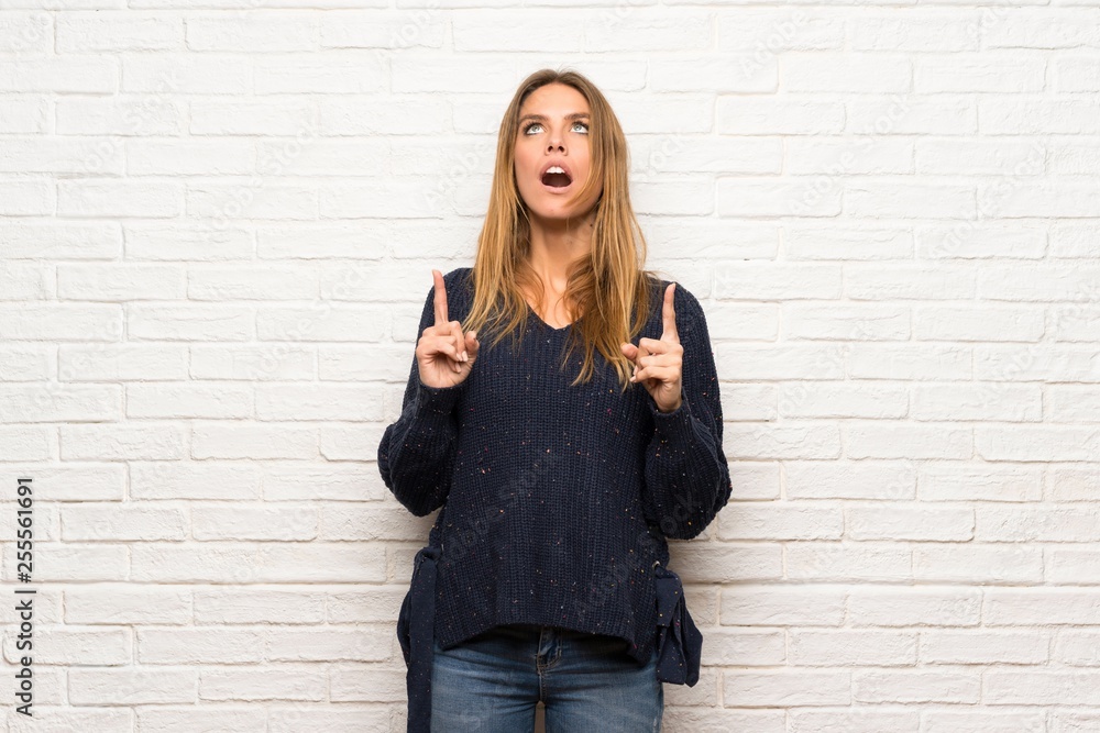 Blonde woman over brick wall surprised and pointing up Blonde woman over brick wall surprised and pointing up