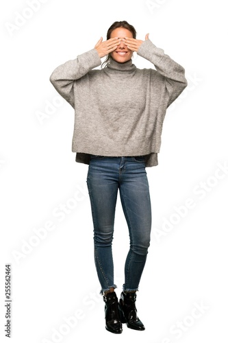 A full-length shot of a Blonde woman with turtleneck covering eyes by hands. Surprised to see what is ahead over isolated white background