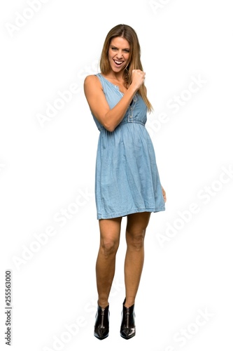 A full-length shot of a Blonde woman with jean dress smiling a lot over isolated white background