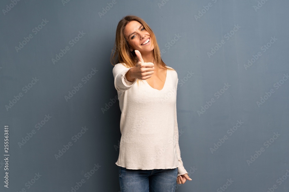 Blonde woman over grey background with thumbs up because something good has happened Blonde woman over grey background with thumbs up because something good has happened