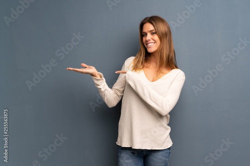 Blonde woman over grey background holding copyspace imaginary on the palm to insert an ad