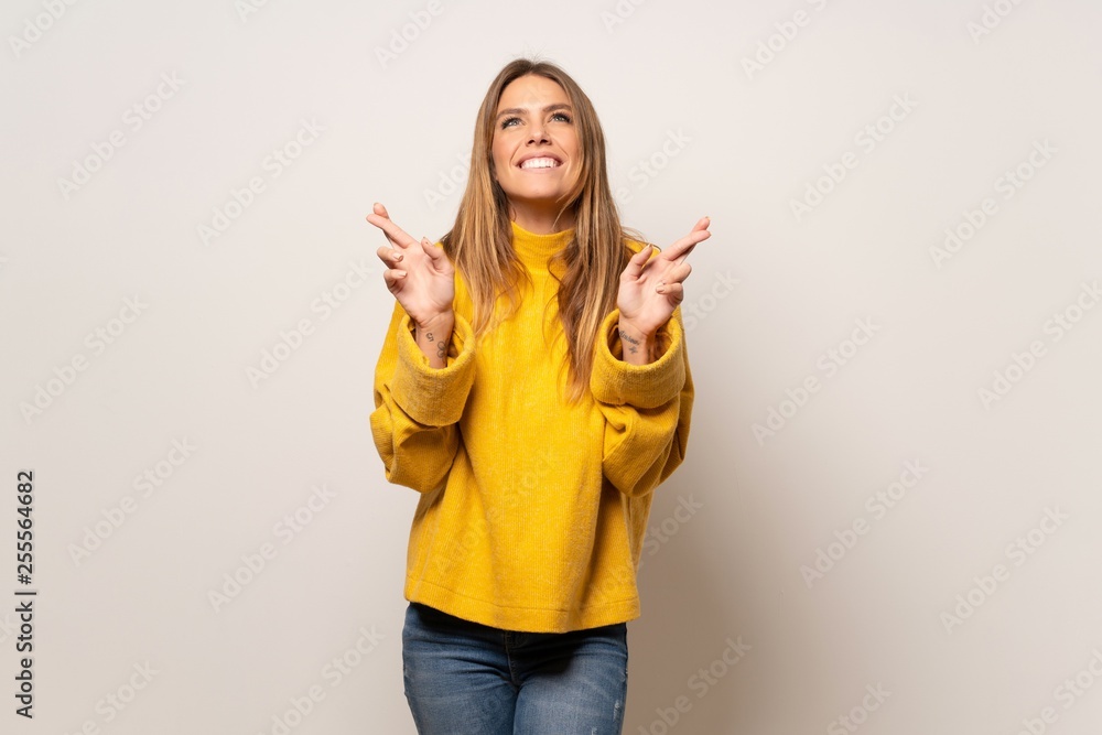 Woman with yellow sweater over isolated wall with fingers crossing and wishing the best Woman with yellow sweater over isolated wall with fingers crossing and wishing the best
