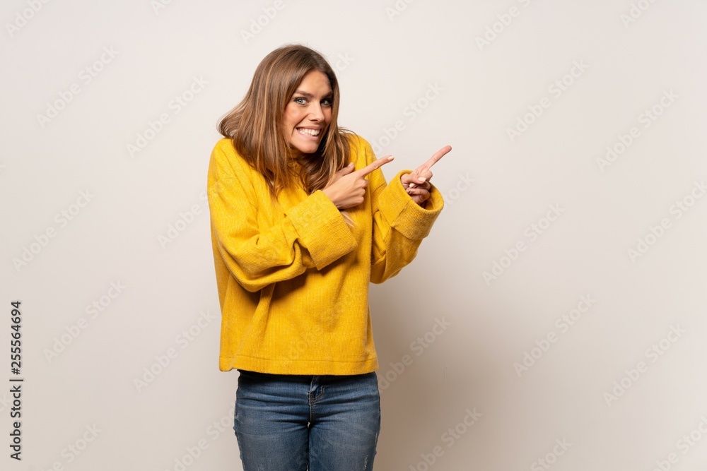 Woman with yellow sweater over isolated wall frightened and pointing to the side Woman with yellow sweater over isolated wall frightened and pointing to the side