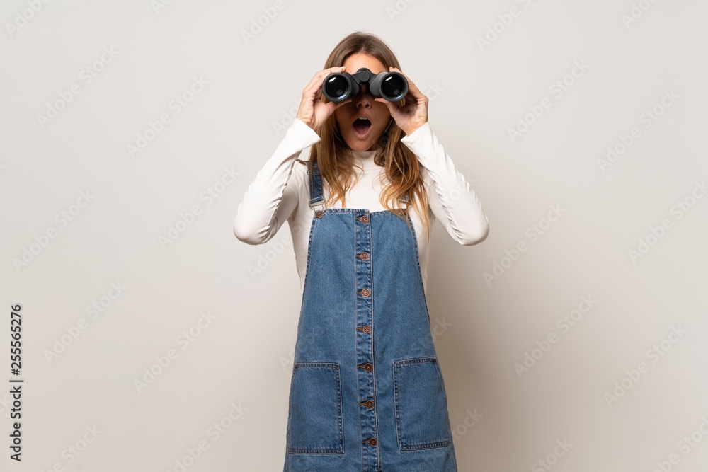 Beautiful woman over isolated white wall and looking in the distance with binoculars Beautiful woman over isolated white wall and looking in the distance with binoculars