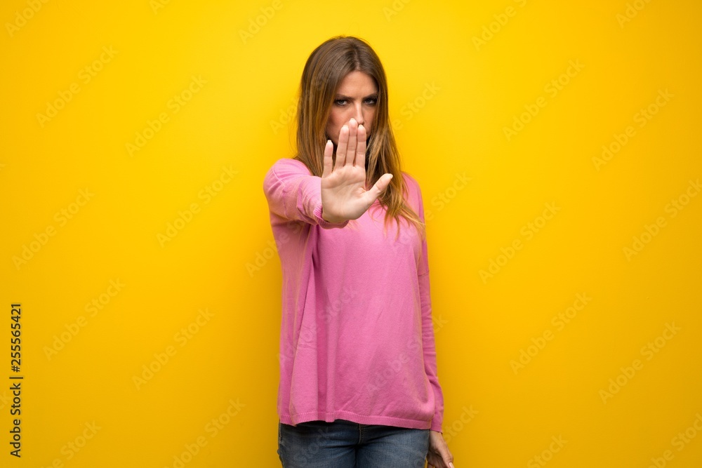 Woman with pink sweater over yellow wall making stop gesture denying a situation that thinks wrong Woman with pink sweater over yellow wall making stop gesture denying a situation that thinks wrong