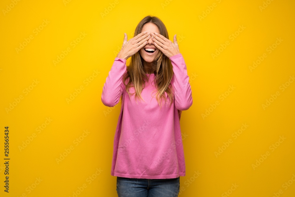 Woman with pink sweater over yellow wall covering eyes by hands. Surprised to see what is ahead Woman with pink sweater over yellow wall covering eyes by hands. Surprised to see what is ahead