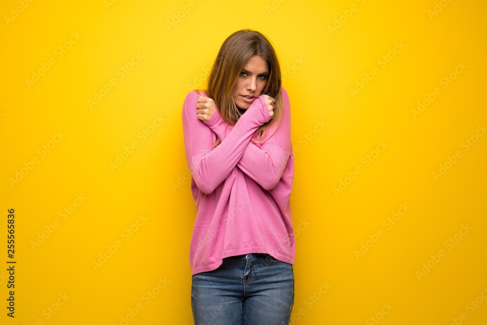 Woman with pink sweater over yellow wall freezing Woman with pink sweater over yellow wall freezing