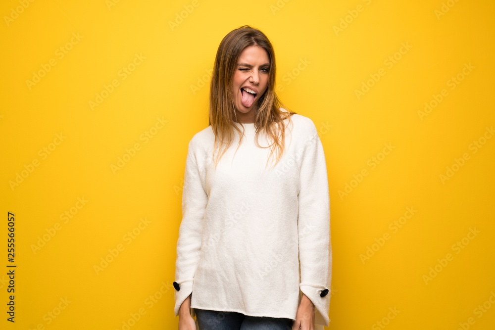 Blonde woman over yellow wall showing tongue at the camera having funny look Blonde woman over yellow wall showing tongue at the camera having funny look