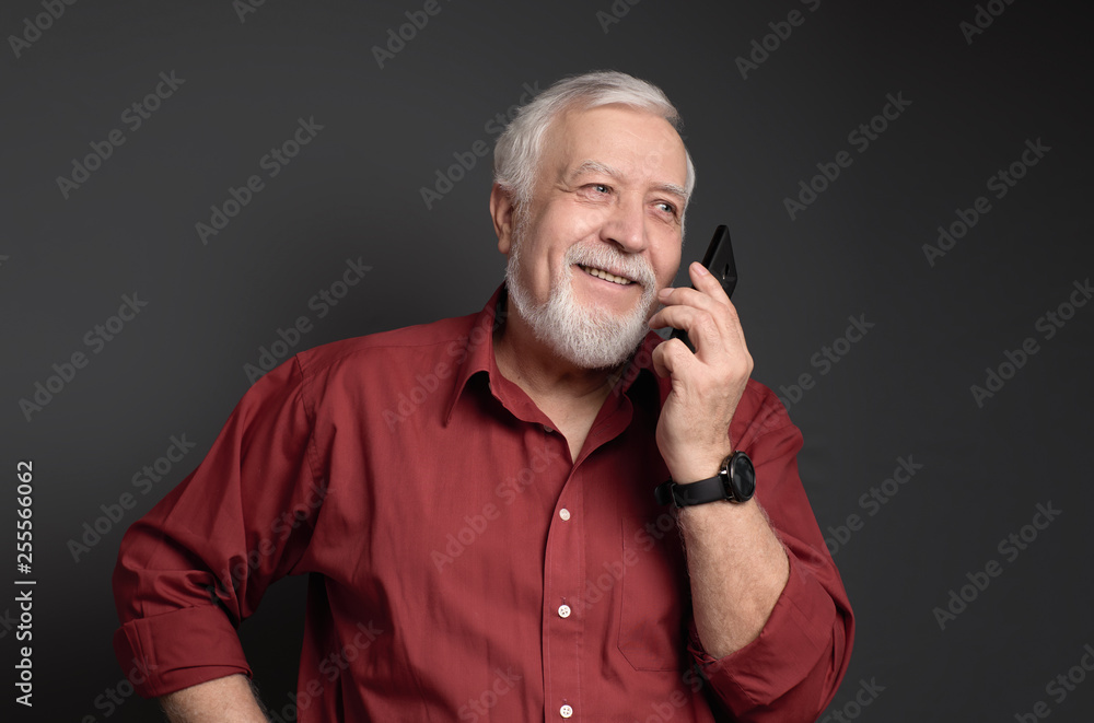 business-haired, gray-haired man in a red shirt is talking to the phone and laughing on a gray background business-haired, gray-haired man in a red shirt is talking to the phone and laughing on a gray background