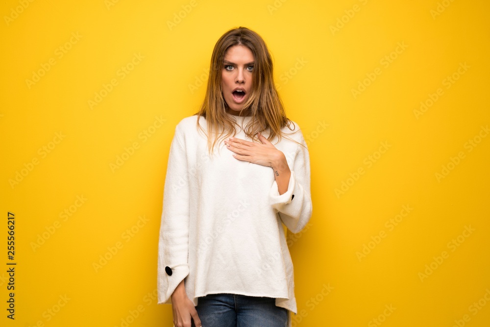 Blonde woman over yellow wall surprised and shocked while looking right Blonde woman over yellow wall surprised and shocked while looking right