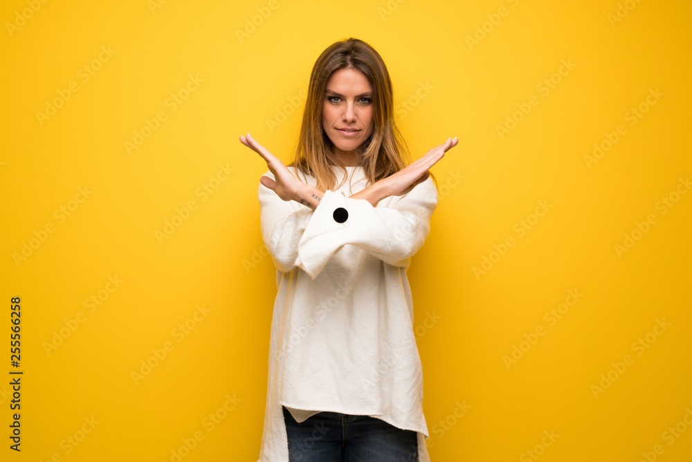 Blonde woman over yellow wall making NO gesture Blonde woman over yellow wall making NO gesture
